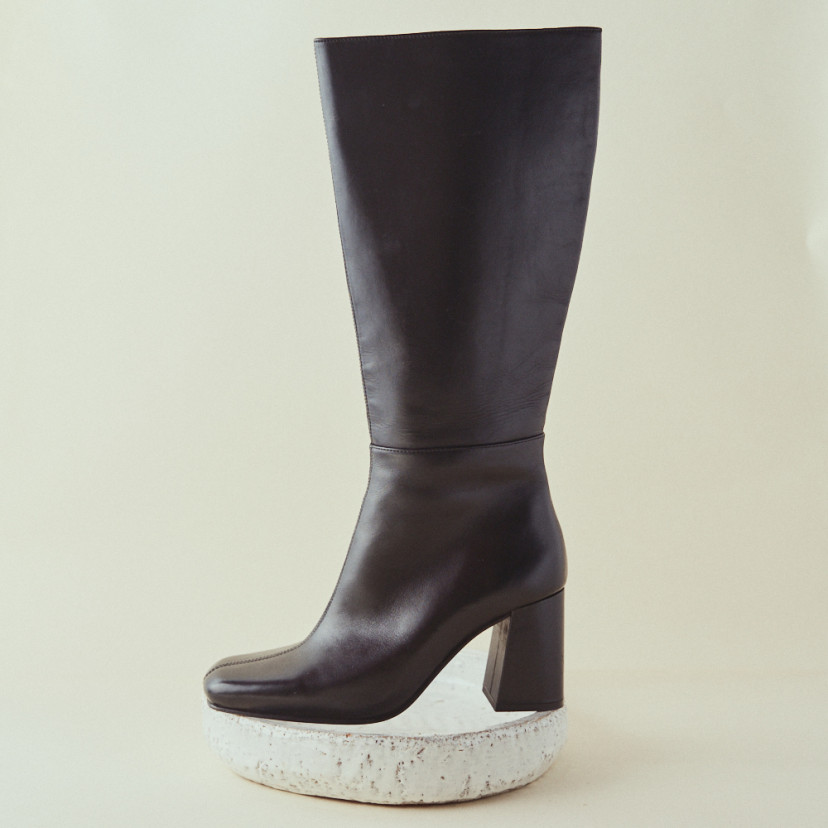 Black leather high-heeled boots with side view in close-up resting on a stone - MONPIEL