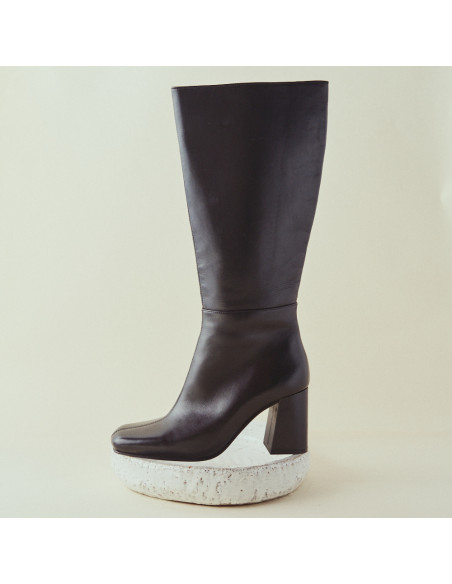 Schwarzer Lederstiefel mit hohem Schaft und Absatz, Profilansicht, Nahaufnahme, auf einem Stein abgestützt - MONPIEL