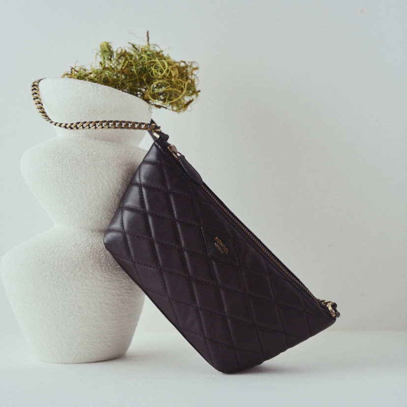 Small women's leather quilted New York bag in black with front view resting on a vase - MONPIEL