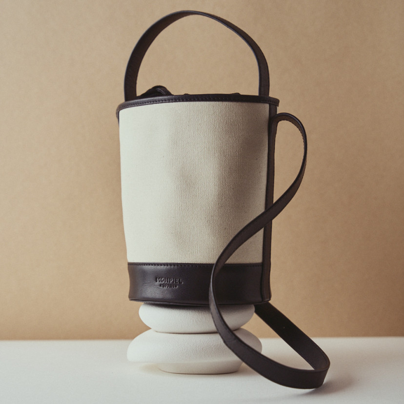 Bolsa pequena tipo bucket em canvas preta, apoiada sobre decoração - MONPIEL