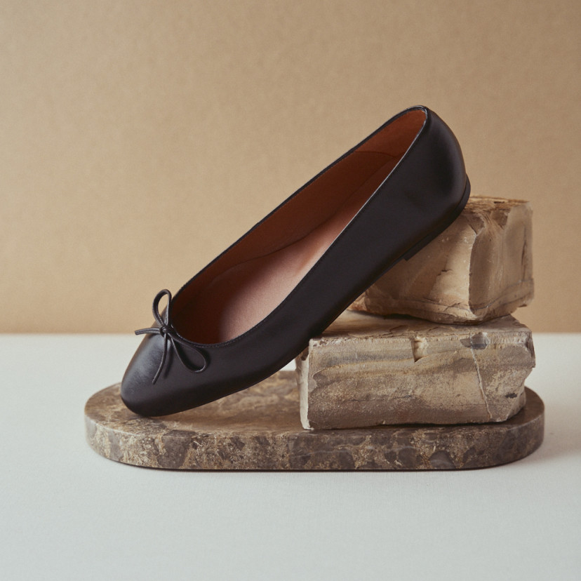 Manolita pointed-toe ballerina in black with perspective view, resting on a stone in close-up - MONPIEL