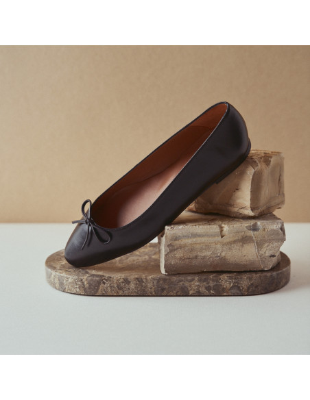 Manolita pointed-toe ballerina in black with perspective view, resting on a stone in close-up - MONPIEL Manolita pointed-toe ballerina in black with perspective view, resting on a stone in close-up - MONPIEL