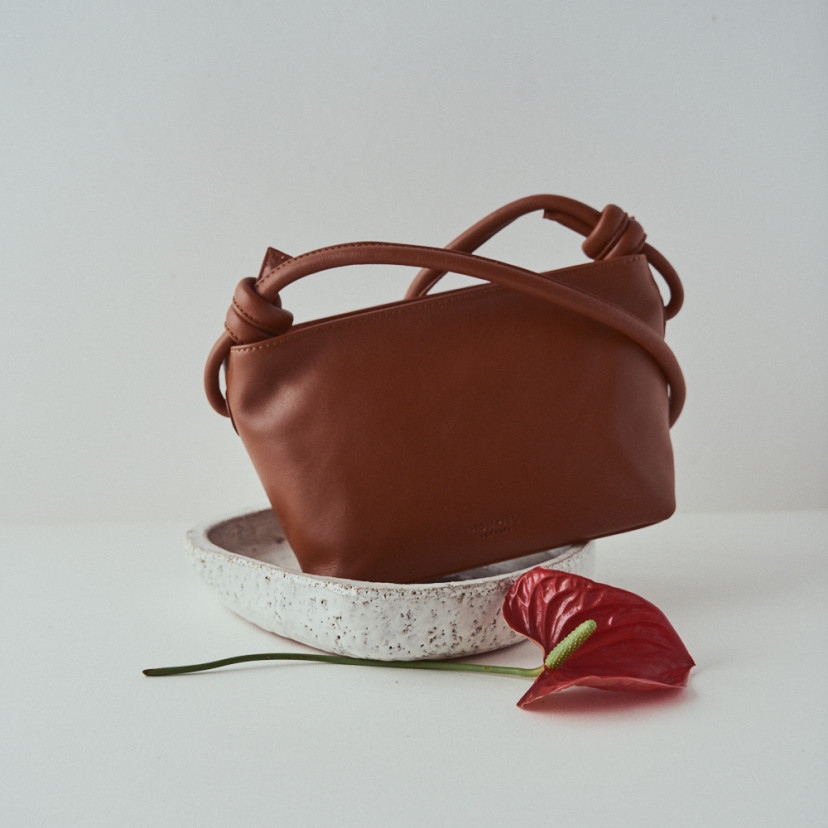 Bolsa pequena de couro com nós na cor couro, inclinada, vista frontal e detalhe de flor - MONPIEL