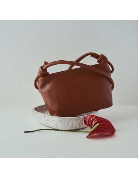 Small tan leather knot bag, tilted, front view, with flower detail - MONPIEL