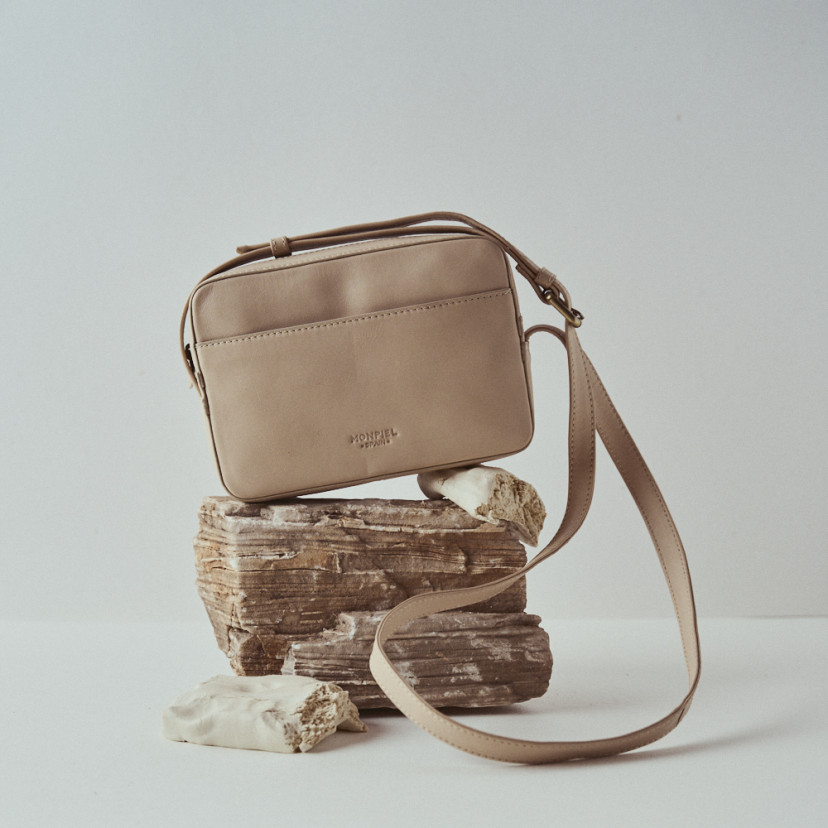 Bolsa de couro na cor bege com detalhe de alça, apoiada sobre pedras - MONPIEL