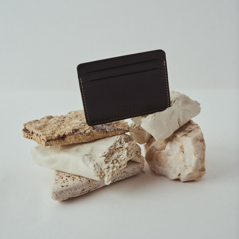 Mini leather cardholder in black with front view on rocks - MONPIEL