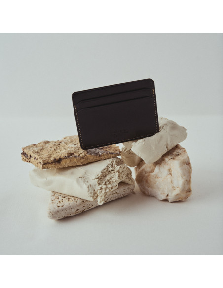 Mini black leather cardholder, front view, placed on rocks - MONPIEL Mini black leather cardholder, front view, placed on rocks - MONPIEL
