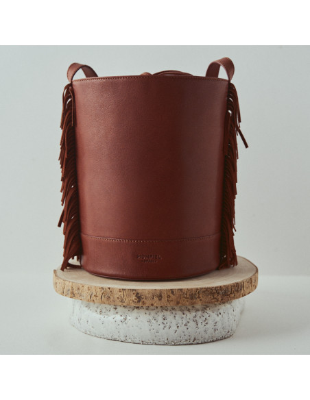 Bolsa de couro grande tipo bucket com franjas Roma na cor couro, close-up, vista frontal, apoiada em madeira - MONPIEL