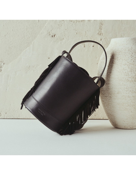 Kleine schwarze Leder-Bucketbag Roma mit Fransen, Frontalansicht, auf einem Vase abgestützt - MONPIEL