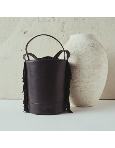 Kleine schwarze Leder-Bucketbag Roma mit Fransen, Frontalansicht, neben einer Vase - MONPIEL