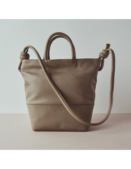 Large leather knot bag in taupe with front view and handle detail, wall background - MONPIEL Large leather knot bag in taupe with front view and handle detail, wall background - MONPIEL