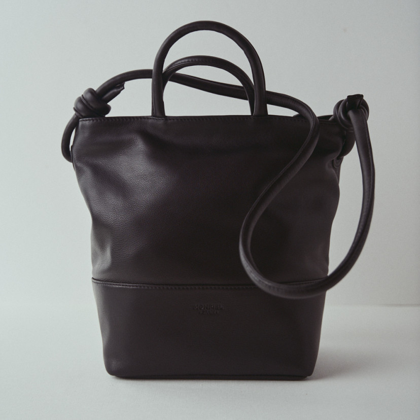 Bolsa grande de couro com nós na cor preta, vista frontal com fundo de parede - MONPIEL