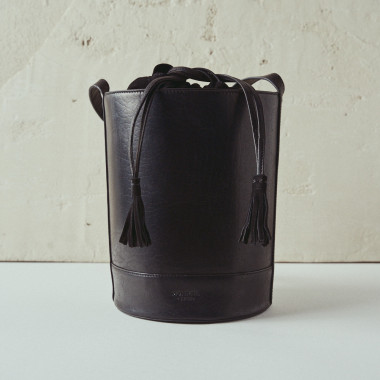 Bolso redondo en forma de cubo de piel en color negro con vista frontal, fondo pared - MONPIEL