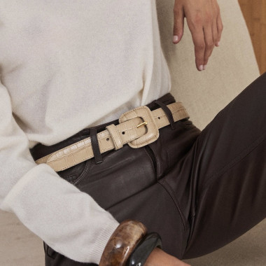 Belt with crocodile-embossed leather covered buckle in sand colour over chocolate brown leather trousers, model seated - MONPIEL 2