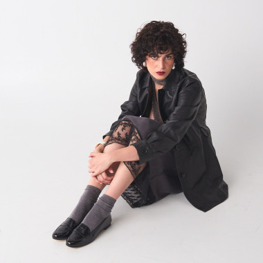 Black patent leather loafer, perspective view, model seated on the floor in a full shot - MONPIEL