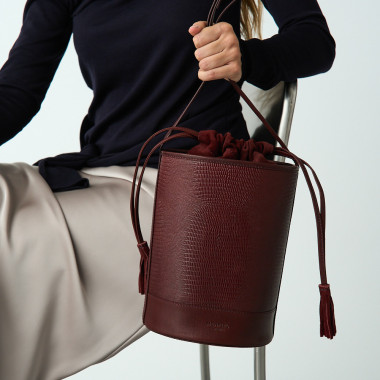 Bolsa redonda em formato de balde de couro na cor preta, vista frontal com fundo de parede - MONPIEL 2