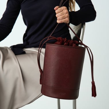 Round black leather bucket-style bag, front view, with wall background - MONPIEL 2