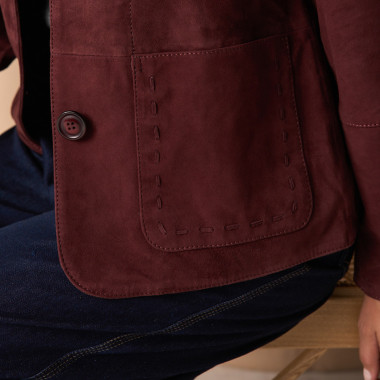 Veste en cuir camel avec détails de coutures, posée sur les épaules, vue de profil, plan large du modèle assis sur une - MONPIEL 2