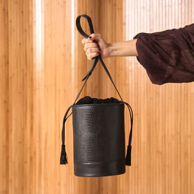 Round black leather bucket-style bag, front view, with wall background - MONPIEL 2