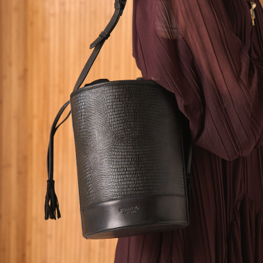 Bolsa redonda em formato de balde de couro na cor preta, vista frontal com fundo de parede - MONPIEL 2