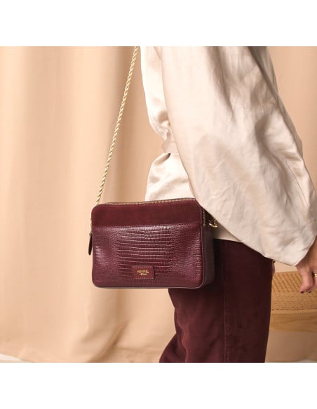 Bolsa tiracolo com corrente dourada combinando pele de serpente e camurça bordô ao ombro da modelo em plano médio - MONPIEL