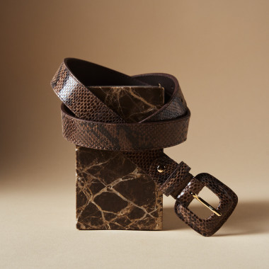 Belt with crocodile-embossed leather covered buckle in sand colour over chocolate brown leather trousers, model seated - MONPIEL 2