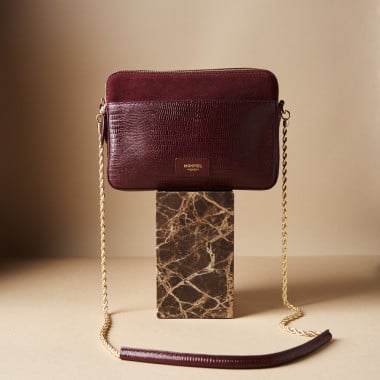Bolsa em pele de serpente e camurça bordô com corrente dourada sobre pedra de mármore em plano geral frontal - MONPIEL