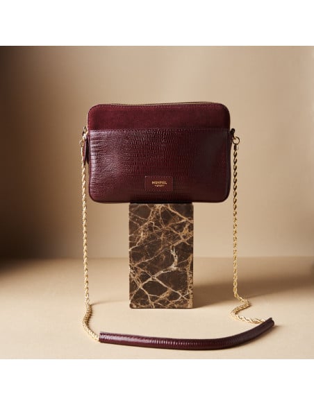 Bolsa em pele de serpente e camurça bordô com corrente dourada sobre pedra de mármore em plano geral frontal - MONPIEL