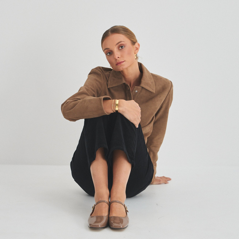 Mary Jane con cinturino Carlota in vernice color cannella, vista frontale, piano generale del modello seduto sul pavim - MONPIEL