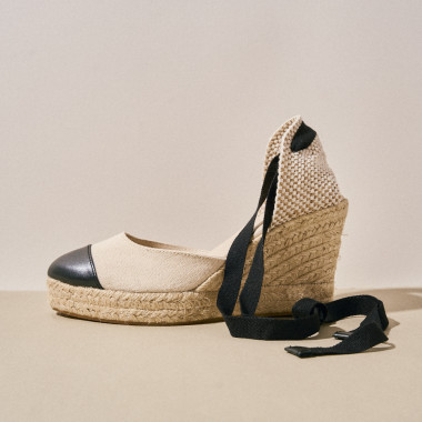 Platinum leather wedge espadrille with black toe cap, close-up shot on a cream-colored surface in side view - MONPIEL