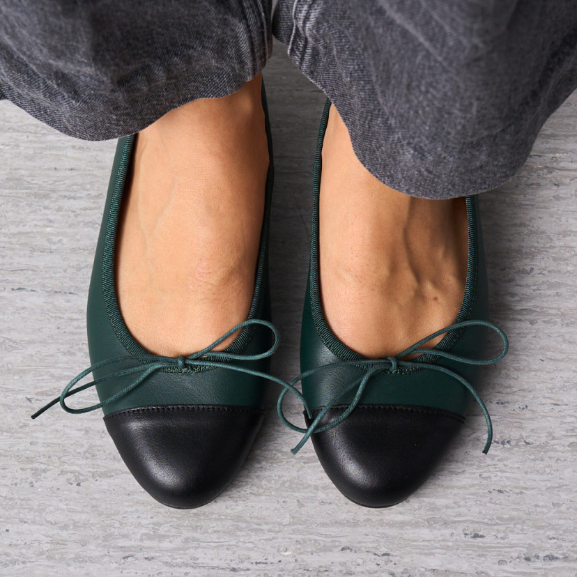 Flache Leder-Ballerinas in Grün mit schwarzer Kappe, Draufsicht mit nebeneinanderstehenden Füßen auf dem Boden – MONPIEL