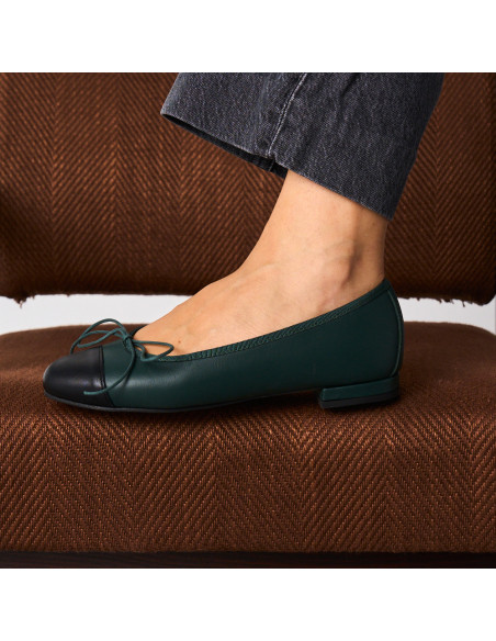Green leather flat ballerinas with black toe cap, side view of one foot resting on a brown armchair - MONPIEL