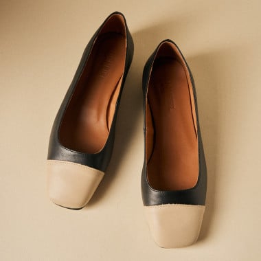 Schuh mit eckiger Spitze in Schwarz und Beige, Seitenansicht mit Hand, die den vom Boden angehobenen Fuß berührt – MONPIEL 2